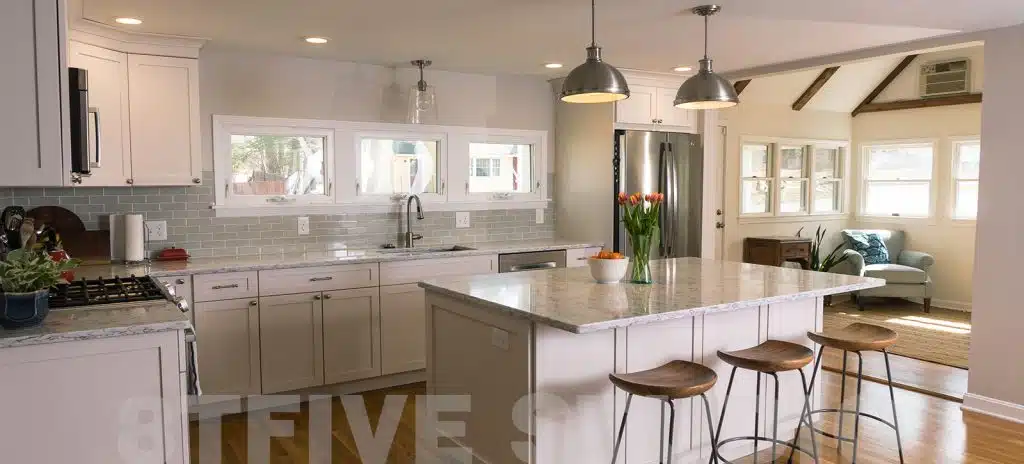 Bright kitchen featuring an island with stools, white cabinets, and a window overlooking the backyard. Quality design by 8TFive.